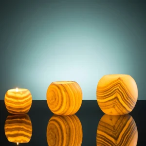 Three alabaster candle holders of varying sizes, illuminated from within, sit on a reflective surface.