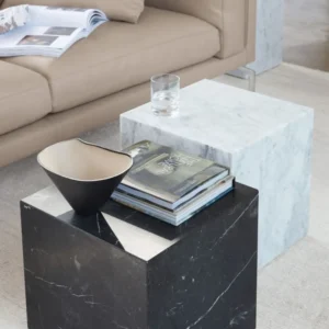 Two marble side tables, one black and one white, hold books and a glass.