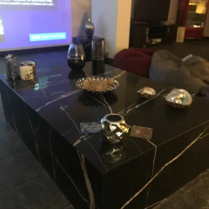 Black marble coffee table with gold veining, displaying decorative items and snacks.