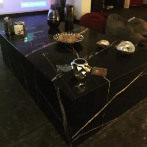 Black marble coffee table with gold veining, displaying decorative items.