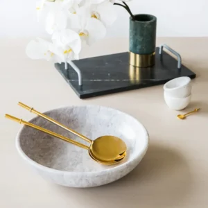 Marble serving bowl with gold salad servers, on a marble tray with orchids.