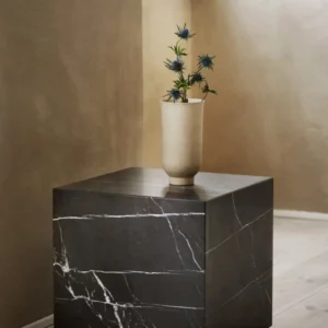 Beige ceramic vase with blue thistle flowers sits on a dark marble cube.