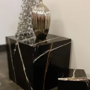 Black marble nesting tables with gold veining, displaying a silver vase and decorative beads.