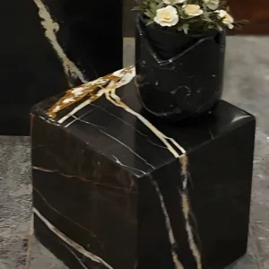 Black marble pedestal with gold veining, holding a black marble vase of white flowers.