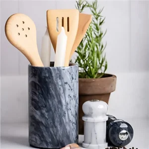 Gray marble utensil holder with wooden cooking spoons and candles.