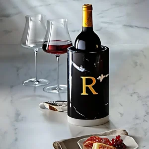 Black marble wine cooler with gold 'R' initial, holding a bottle of red wine; two wine glasses nearby.